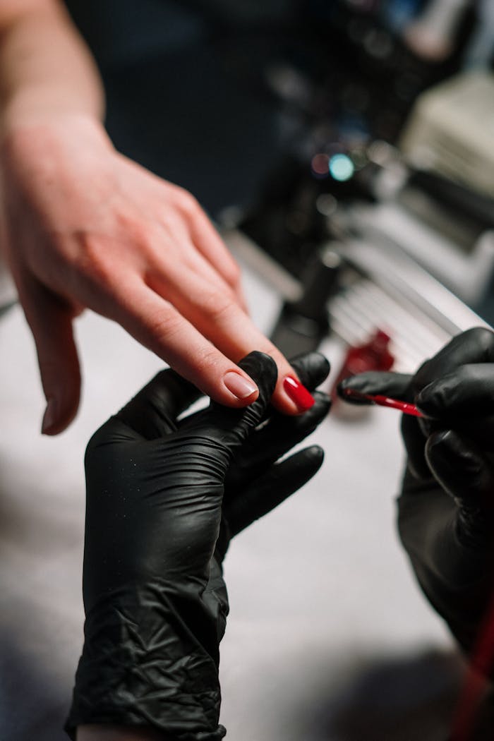 services-05 Close-up of a nail artist applying polish with precision using black gloves in a salon setting.
