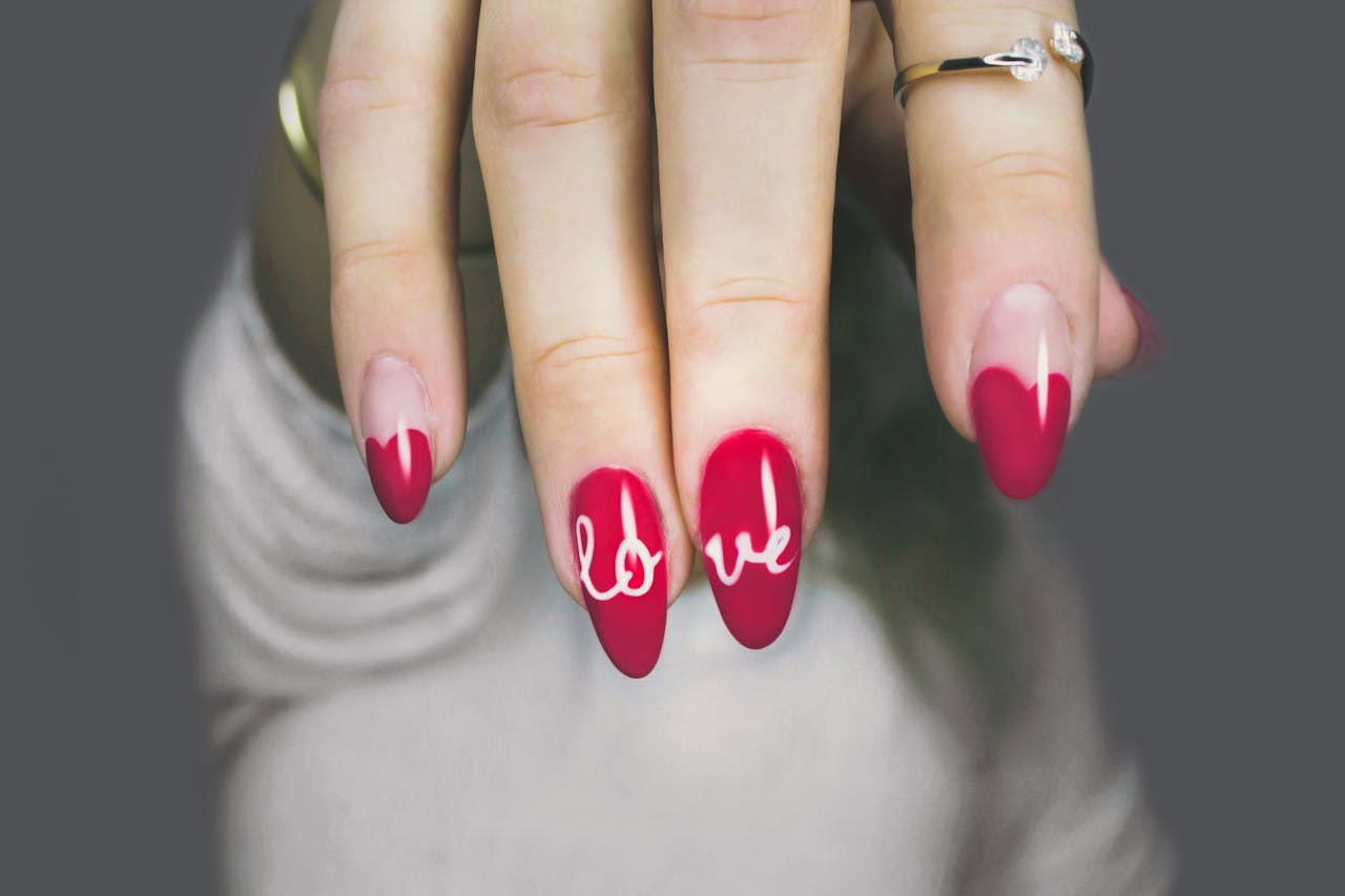 home-hero Vibrant red nails with 'love' art on a woman's hand, showcasing elegant style and design.